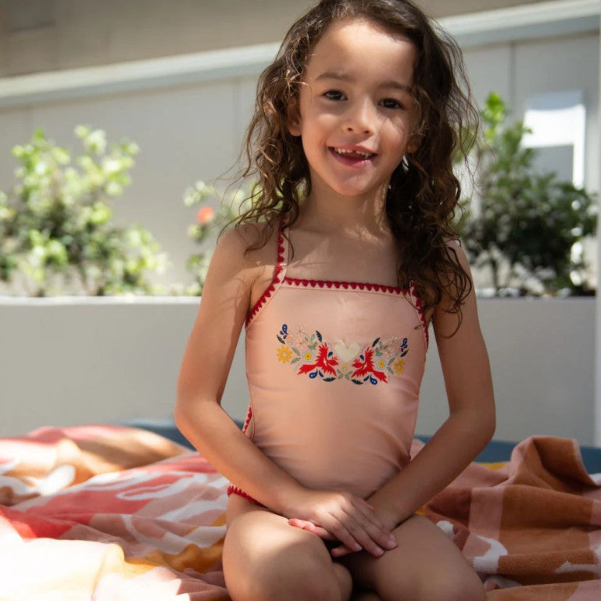 Young girl wearing the Tyoub vanilla fire bird embroidered swimsuit outdoors showing front view.