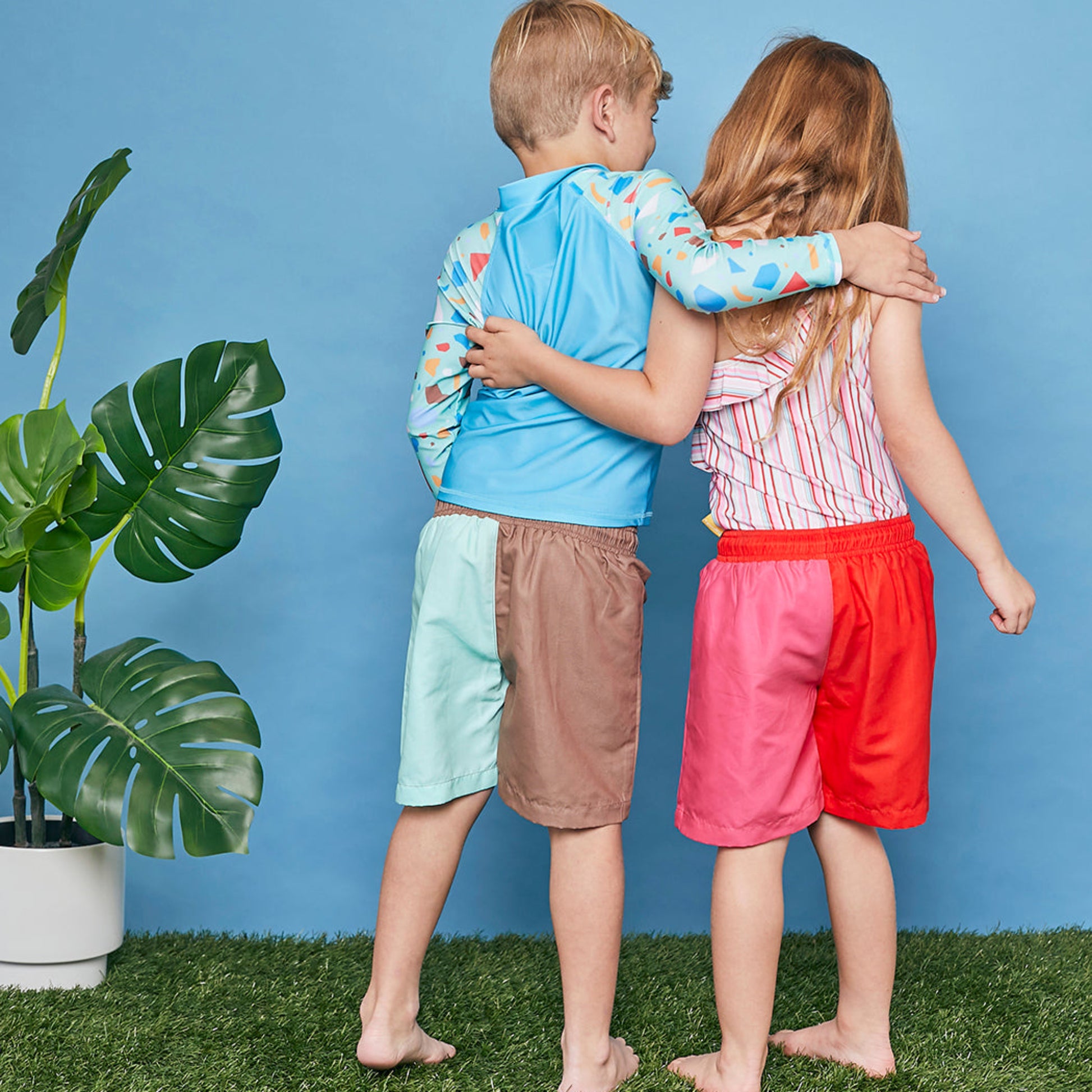Young boy wearing a Tyoub long sleeve turquoise ocean glass rashie and matching board shorts in a studio setting.