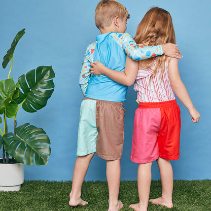 Young boy wearing a Tyoub long sleeve turquoise ocean glass rashie and matching board shorts in a studio setting.