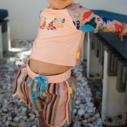 Young boy wearing Tyoub multi coloured recycled swim shorts and matching long sleeve rash top on an Australian beach.