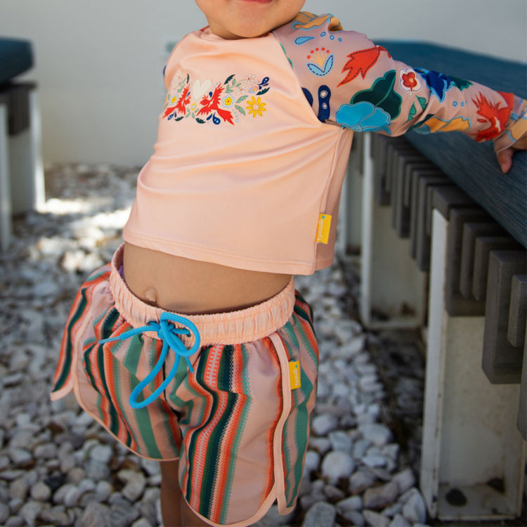Young boy wearing Tyoub multi coloured recycled swim shorts and matching long sleeve rash top on an Australian beach.