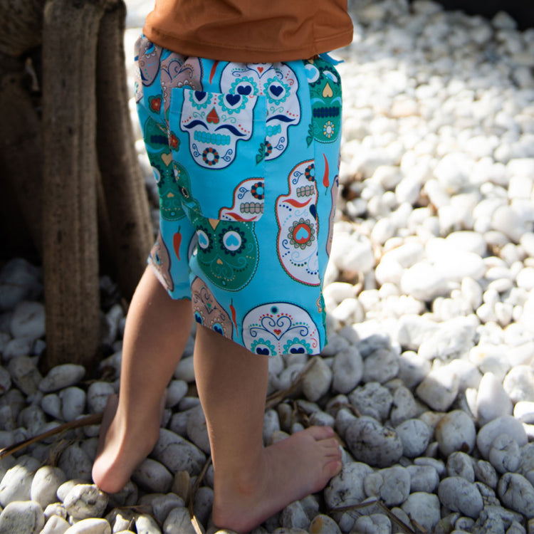 Side angle view of a child wearing eco-friendly recycled material board shorts near a pool.