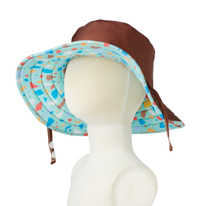 The alternate side configuration of the kids wide brim sun hat showing a solid tortoise brown crown with a turquoise ocean glass terrazzo print under-brim.