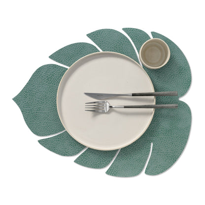 Monstera leaf recycled leather placemat featuring the signature LIND DNA Hippo finish in pastel green with a plate, cup, knife and fork.