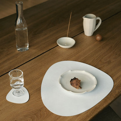 Curve recycled leather placemat featuring the signature LIND DNA Nupo finish on a wooden table with a white plate, glass, and small bowl.