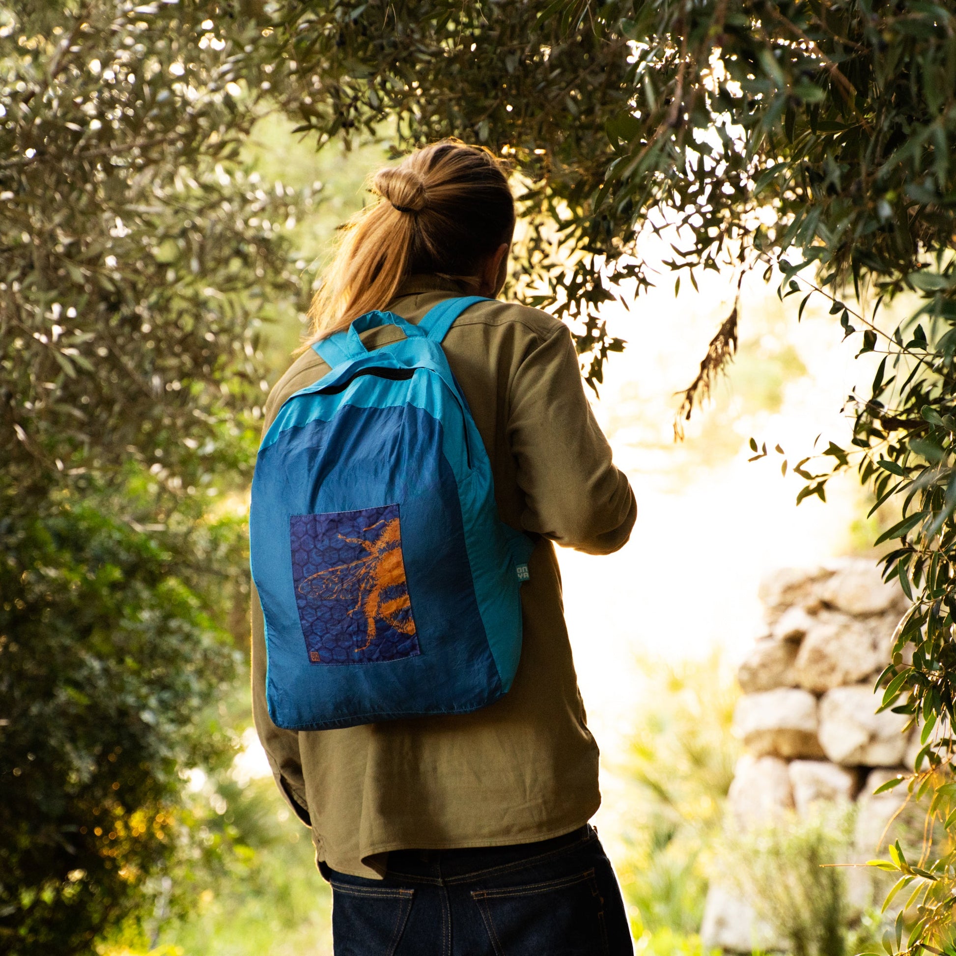 Man carrying an ONYA 100% recycled plastic backpack in a leafy outdoor area