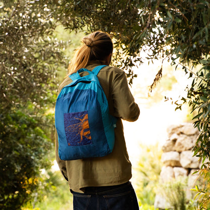 Man carrying an ONYA 100% recycled plastic backpack in a leafy outdoor area