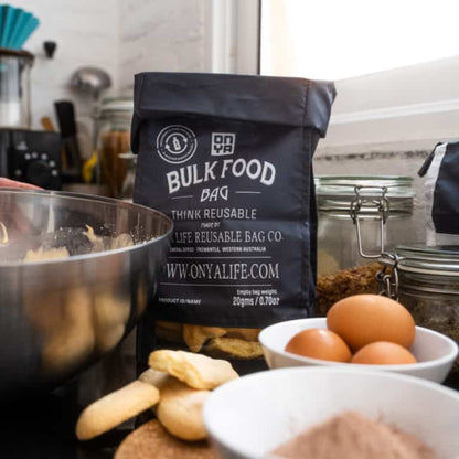 Single Onya large reusable bulk food bag with a clear viewing window and printed tare weight in use in a kitchen with ingredients in charcoal variant.