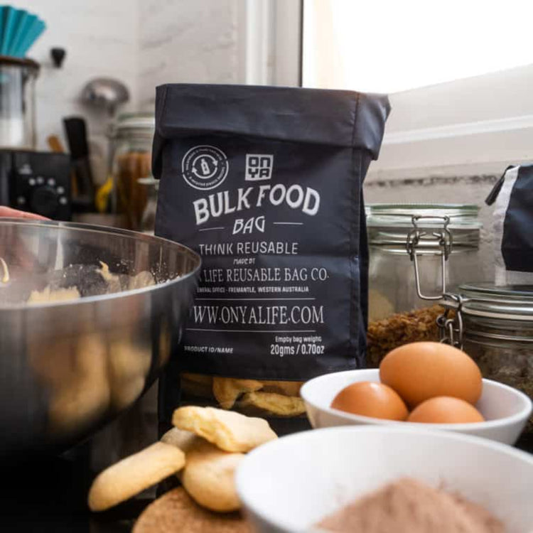 Single Onya large reusable bulk food bag with a clear viewing window and printed tare weight in use in a kitchen with ingredients in charcoal variant.