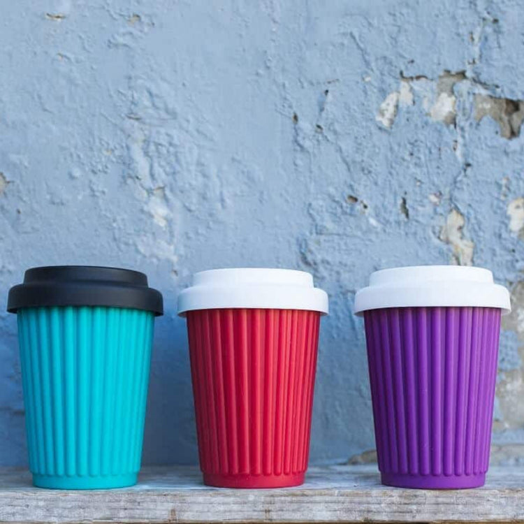 Three Onya replacement coffee cup lids  made from flexible food safe silicone on three reusable ONYA coffee cups in front of a blue wall.