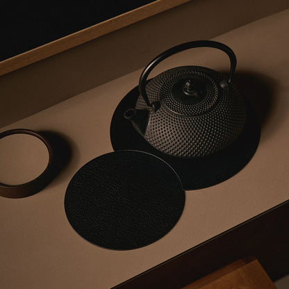 Modern minimalist kitchen benchtop styled with a circular LIND DNA recycled leather hot mat protecting the surface from a hot tea pot.