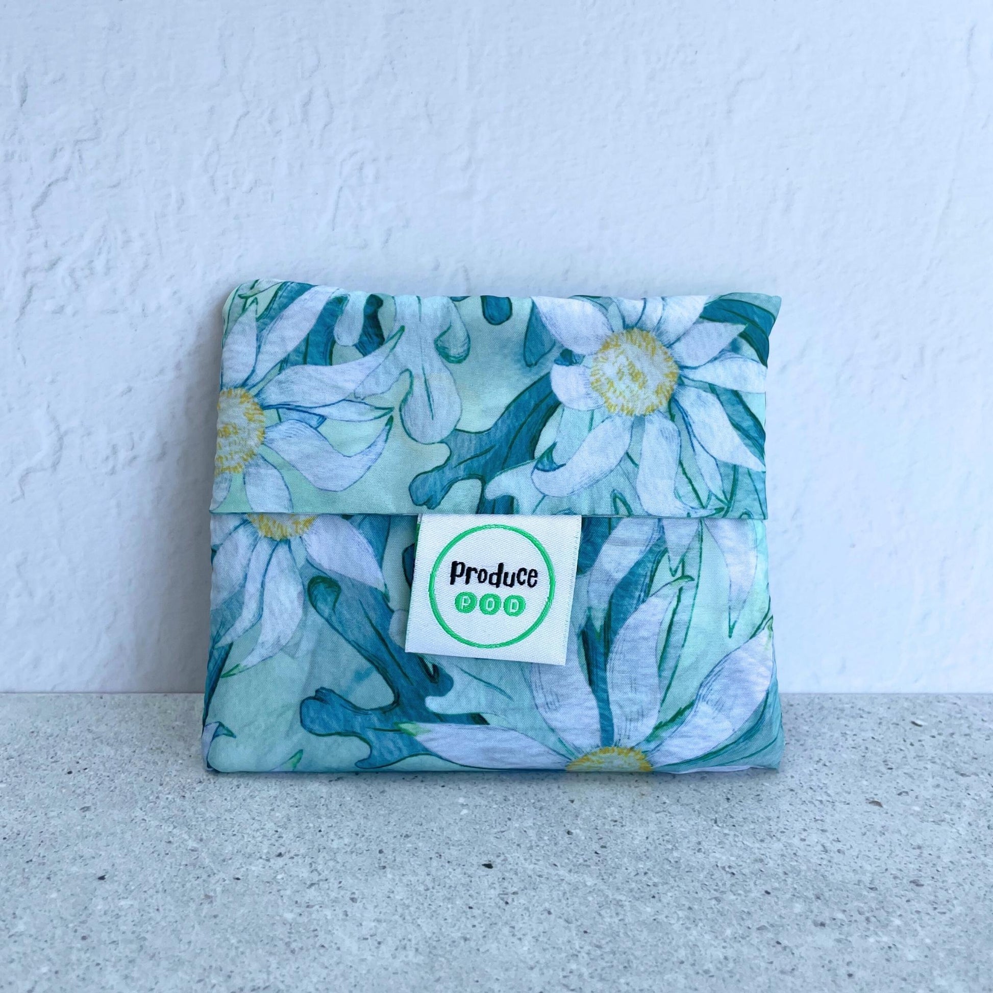 Close up view of the lightweight sixty gram reusable grocery bag folded entirely inside its own integrated self storing travel pouch for compact pocket storage. Flannel flower variant.