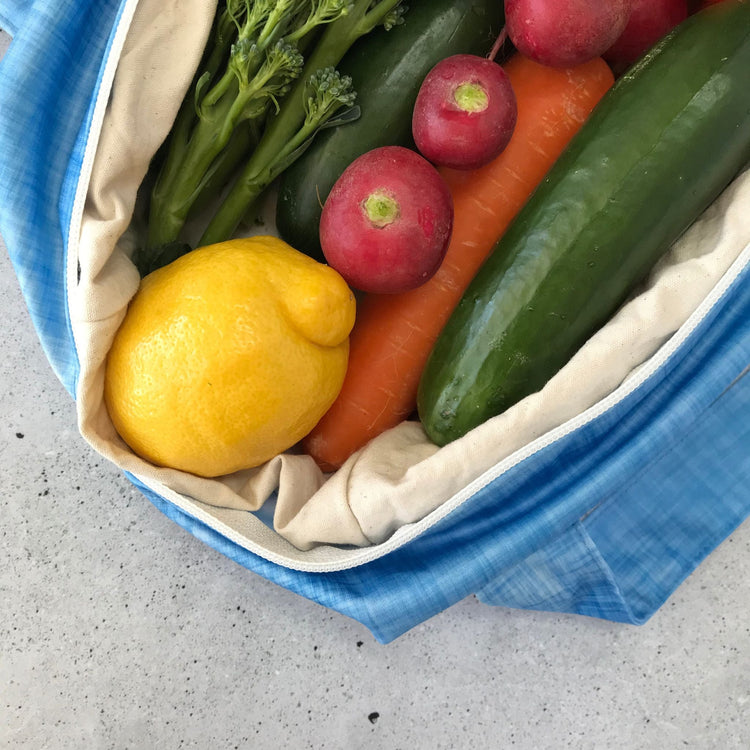 Single Produce Pod reusable veggie storage bag featuring a custom Blueberry print standing open filled with fresh veg and fruit closeup with lemon on a stone background.