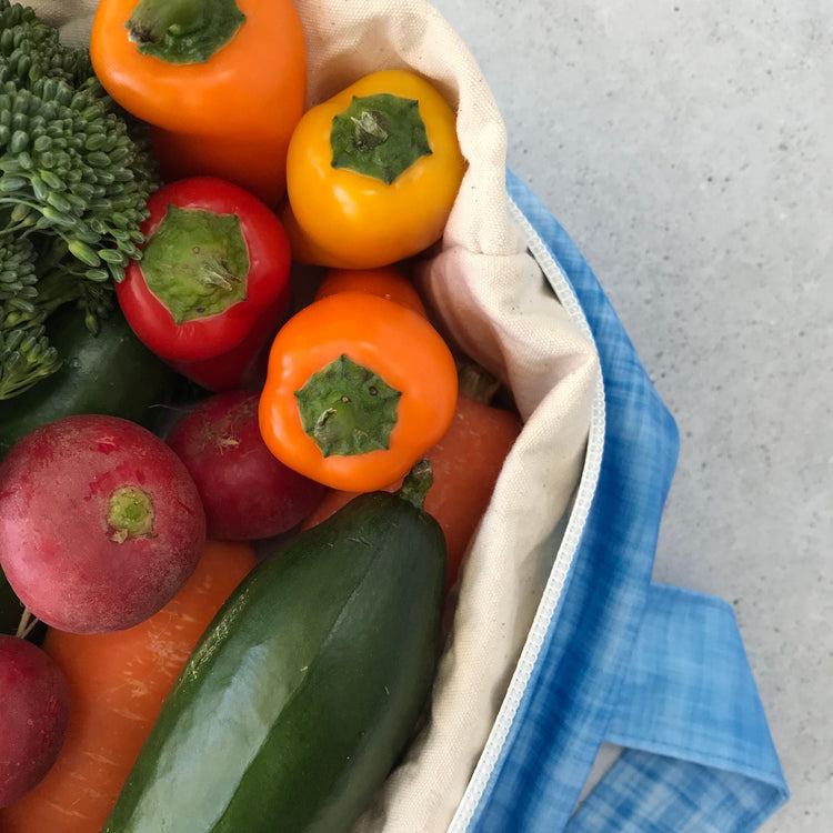Single Produce Pod reusable veggie storage bag featuring a custom Blueberry print standing open filled with fresh veg and fruit closeup with peppers on a stone background.