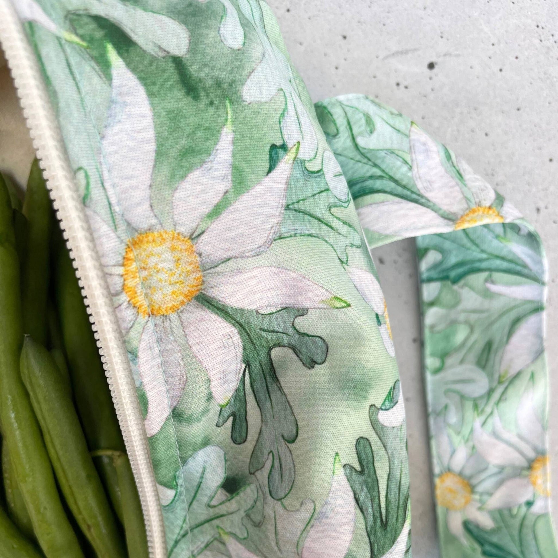 Single Produce Pod reusable veggie storage bag featuring a custom Flannel flower print standing open filled with fresh veg and fruit closeup with beans on a stone background.