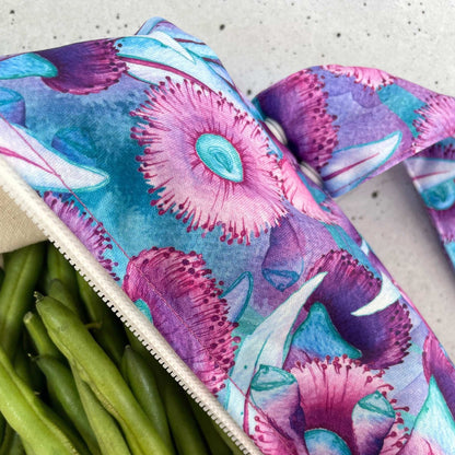 Single Produce Pod reusable veggie storage bag featuring a custom Gum blossom print standing open filled with fresh veg and fruit closeup with beans on a stone background.