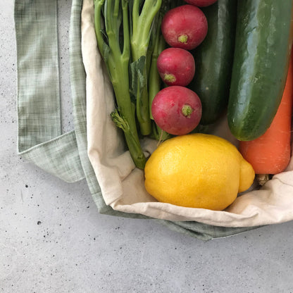 Single Produce Pod reusable veggie storage bag featuring a custom Gum leaf print standing open filled with fresh veg and fruit closeup with lemon on a stone background.
