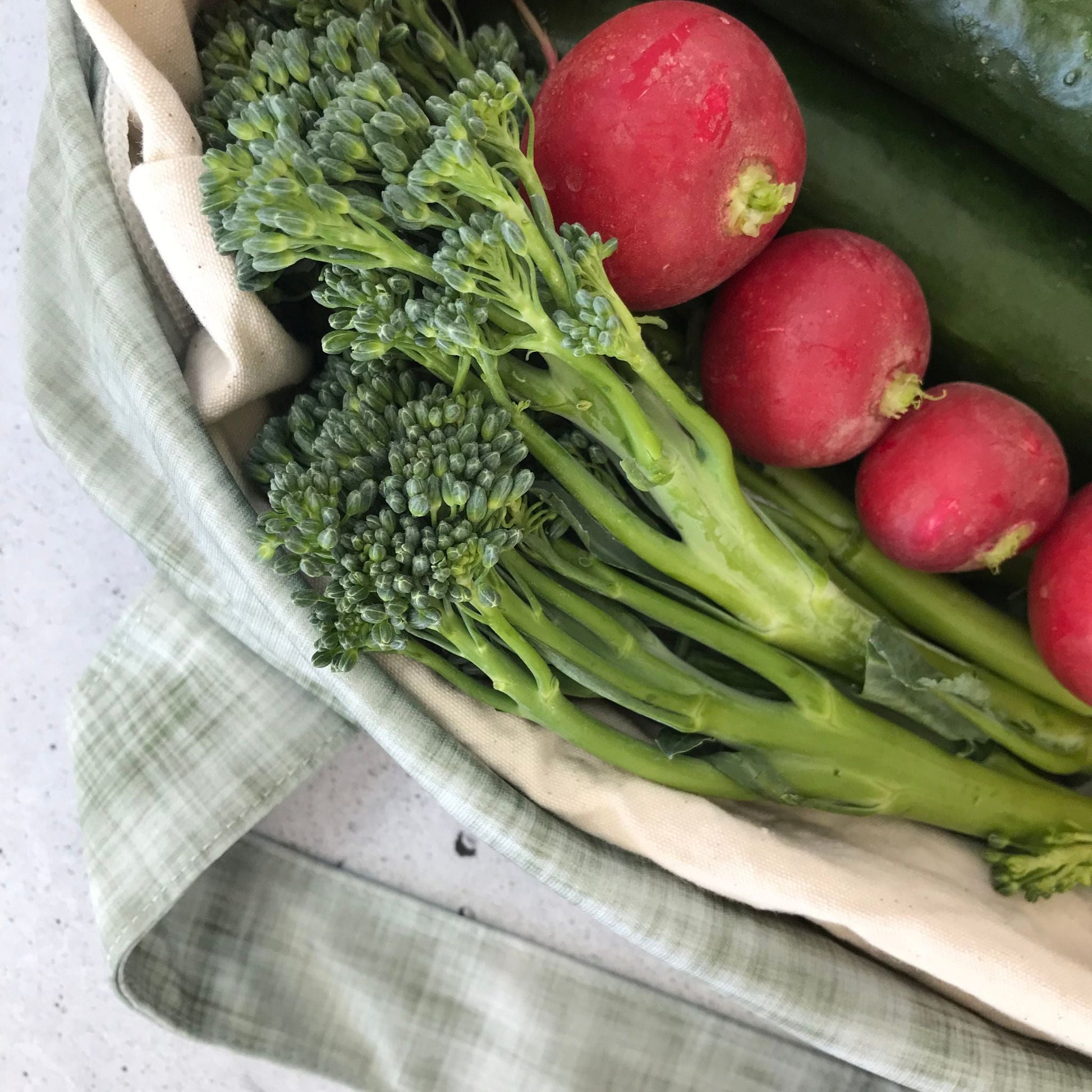Single Produce Pod reusable veggie storage bag featuring a custom Gum leaf print standing open filled with fresh veg and fruit closeup with radish and broccolini on a stone background.