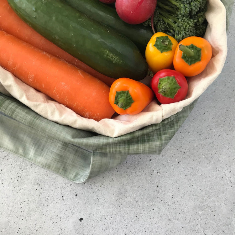 Single Produce Pod reusable veggie storage bag featuring a custom Gum leaf print standing open filled with fresh veg and fruit closeup with carrot, zucchini and peppers on a stone background.