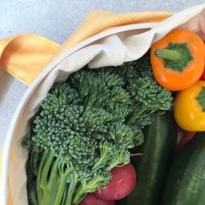 Single Produce Pod reusable veggie storage bag featuring a custom Lemon print standing open filled with fresh veg and fruit closeup with broccolini and peppers on a stone background.