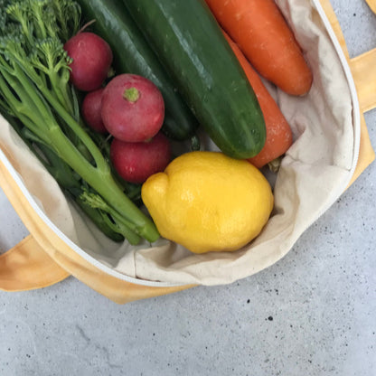 Single Produce Pod reusable veggie storage bag featuring a custom Lemon print standing open filled with fresh veg and fruit closeup with lemon on a stone background.