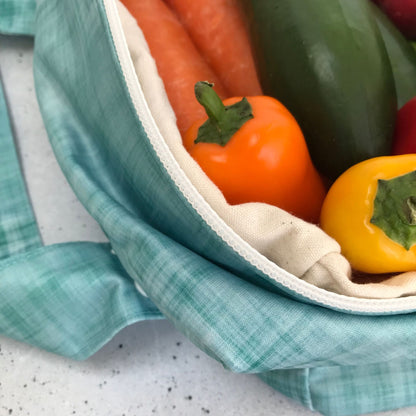 Single Produce Pod reusable veggie storage bag featuring a custom Ocean print standing open filled with fresh veg and fruit closeup with peppers on a stone background.