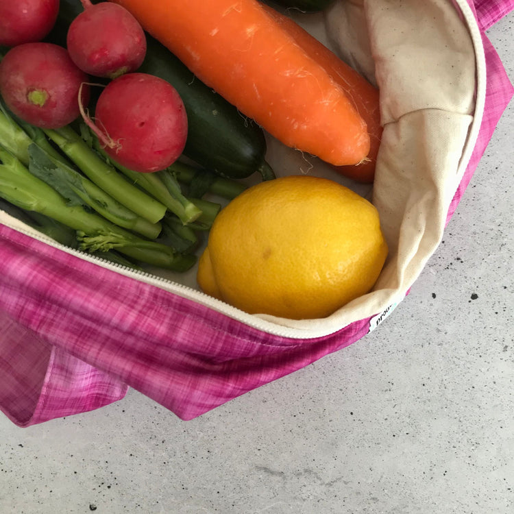 Single Produce Pod reusable veggie storage bag featuring a custom Rhubarb print standing open filled with fresh veg and fruit closeup with lemon on a stone background.