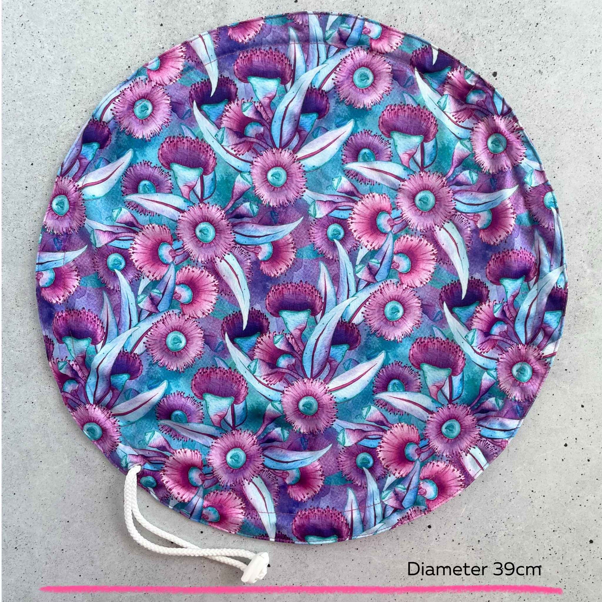 An extra large thirty nine centimeter Produce Pod reusable bowl cover in a Gum blossom print laid out on a surface top view.