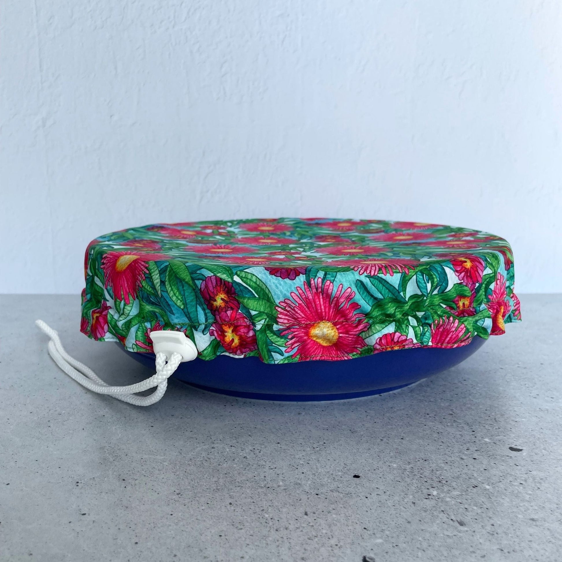 Produce Pod reusable bowl cover in a Sea fig print fitted snugly over a blue serving dish on a stone countertop.
