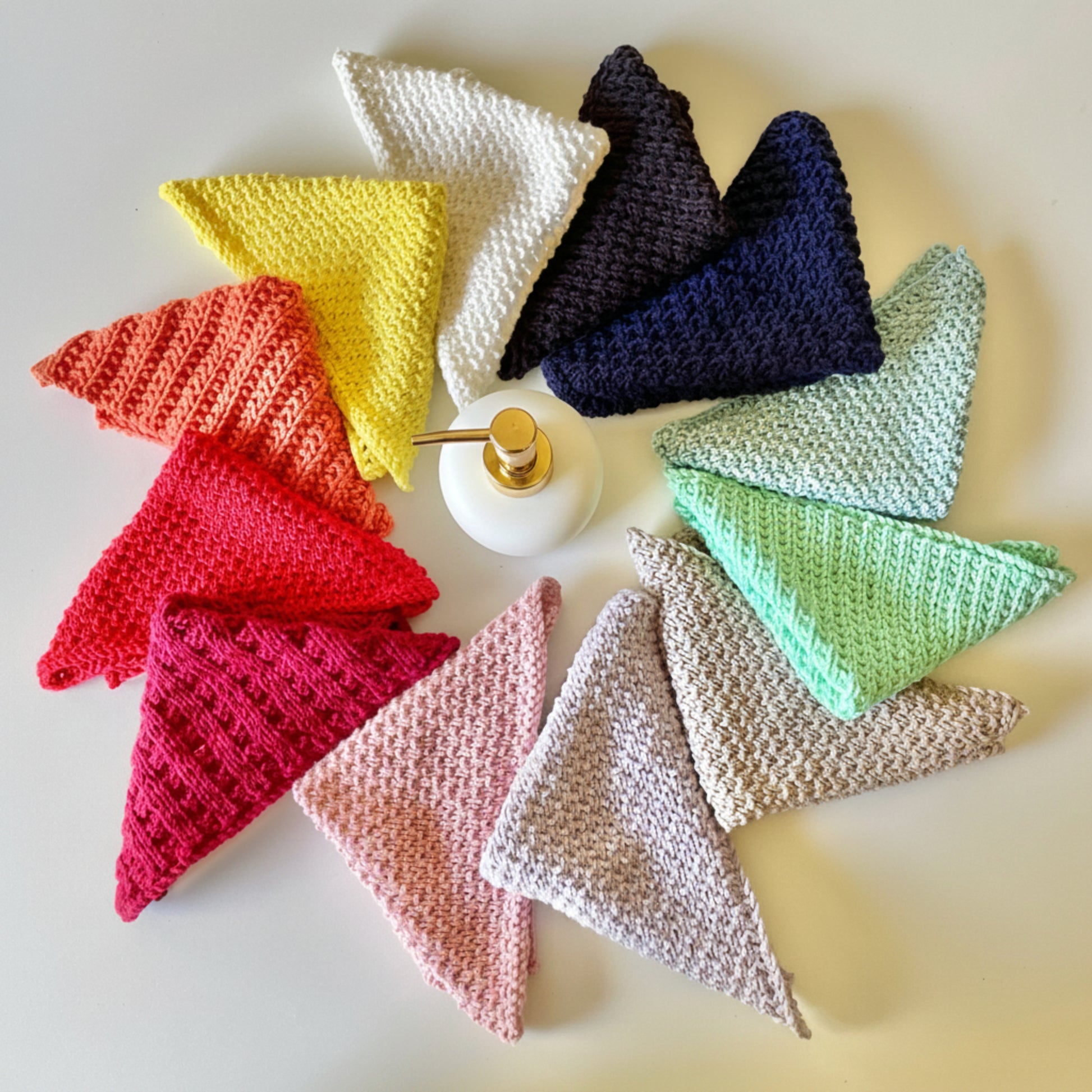 Colourful handmade knitted cloths crafted from 100% recycled cotton for zero-waste home cleaning around a soap bottle.