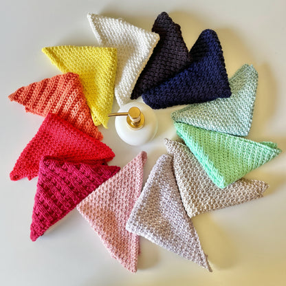Colourful handmade knitted cloths crafted from 100% recycled cotton for zero-waste home cleaning around a soap bottle.