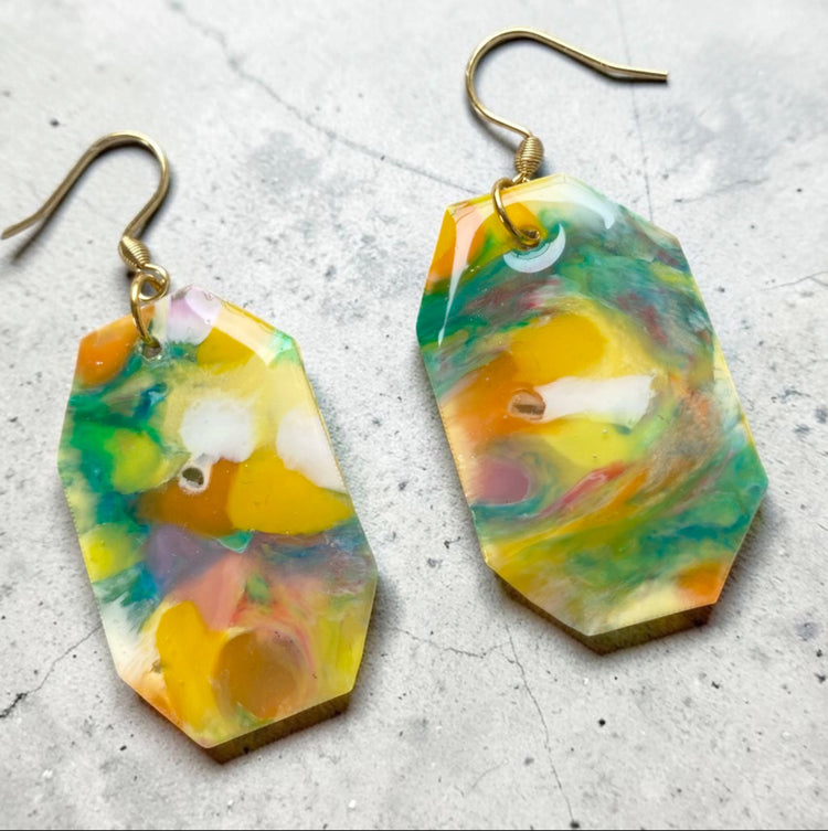 A matching pair of handmade recycled bottle cap statement earrings in a geometric octagon dangle design featuring marbled yellow and green tones.