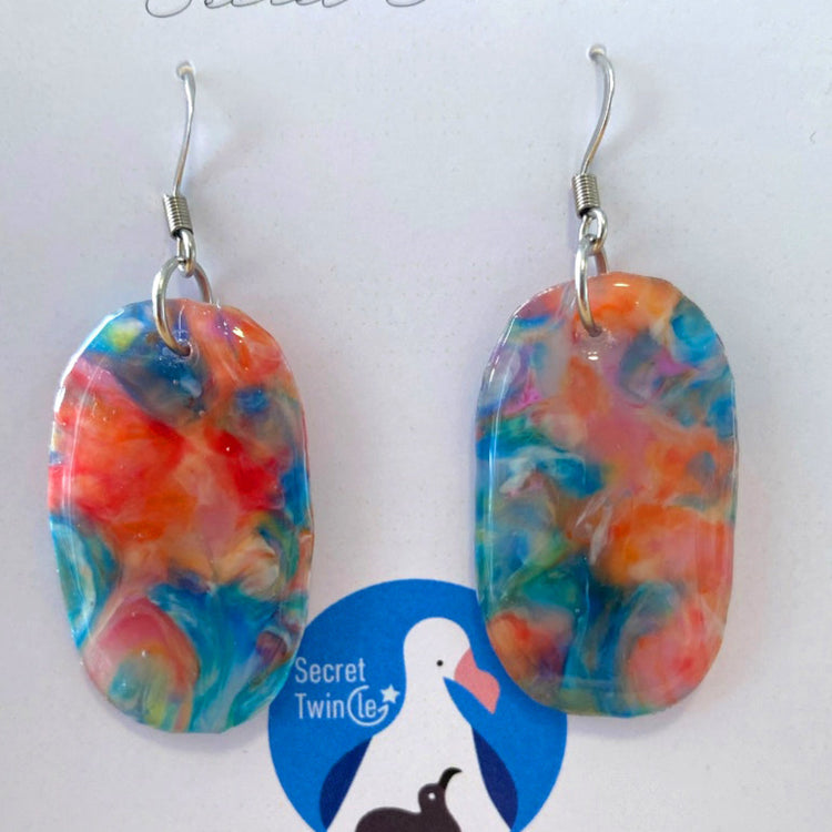 A pair of handmade upcycled plastic statement earrings in a geometric oval dangle design with marbled blue and orange patterns, made in Australia.