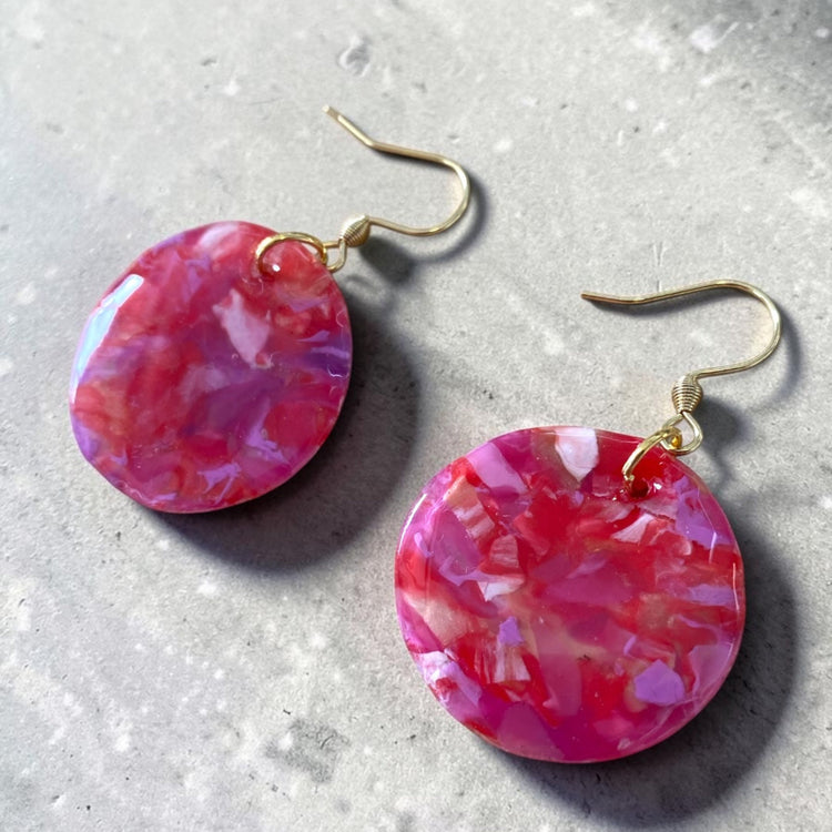 A pair of handmade upcycled plastic statement earrings featuring a geometric round circle dangle design in pink and red, made in Australia.