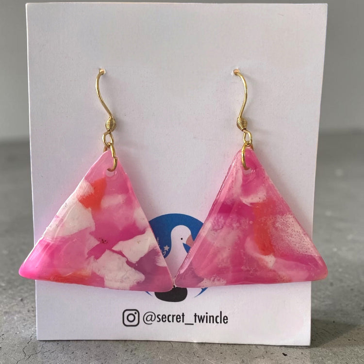 A matching pair of handmade recycled plastic statement earrings in a geometric triangle drop design with marbled pastel pink and white swirls.