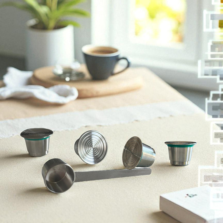 Four Pod Star Nesspresso Original reusable stainless steel coffee pods on a kitchen bench with a scoop and cup of coffee in the background