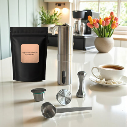 Pod Star barista pack for Nespresso Original line coffee machines featuring two stainless steel reusable pods, a manual coffee grinder, an espresso tamper, a scoop, and premium coffee beans on a kitchen countertop with a cup of coffee.