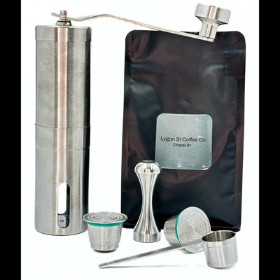 Pod Star barista pack for Nespresso Original line coffee machines featuring two stainless steel reusable pods, a manual coffee grinder, an espresso tamper, a scoop, and premium coffee beans on a white background.