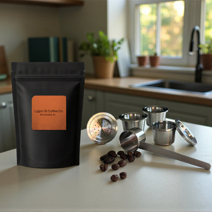Pod Star family pack for Espressotoria coffee machines featuring four stainless steel reusable capsules, an espresso tamper, and a coffee measuring scoop on a .itchen banchtop with coffee beans.