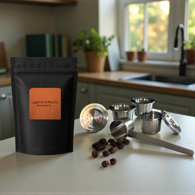 Pod Star family pack for Espressotoria coffee machines featuring four stainless steel reusable capsules, an espresso tamper, and a coffee measuring scoop on a .itchen banchtop with coffee beans.