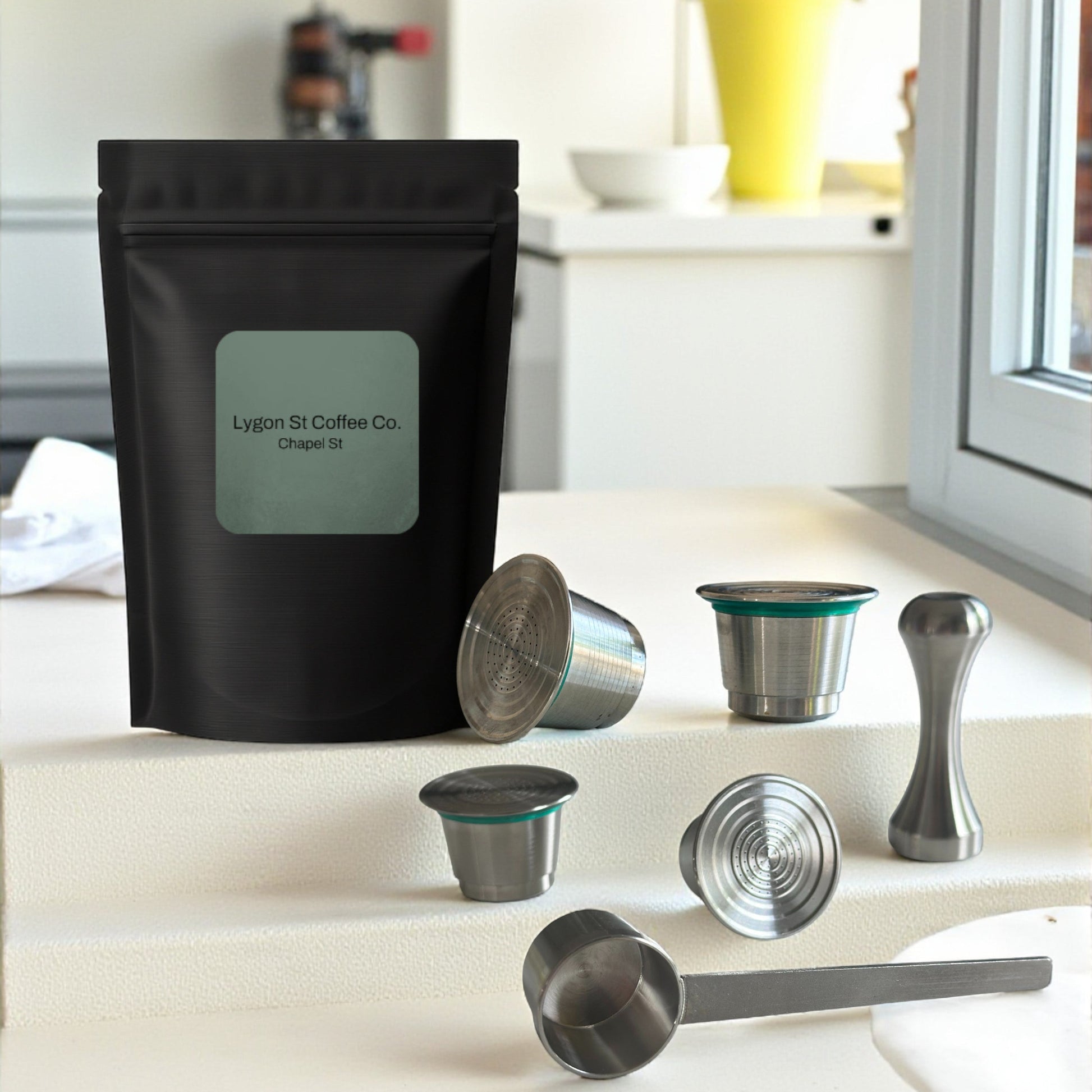 Pod Star family pack for Nespresso Original line coffee machines featuring four stainless steel reusable capsules, an espresso tamper, and a coffee measuring scoop on a kitchen countertop.