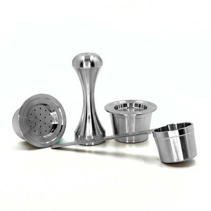 Two refillable stainless steel coffee pods displayed alongside a precision packing tamper and measuring scoop spoon on a white background.