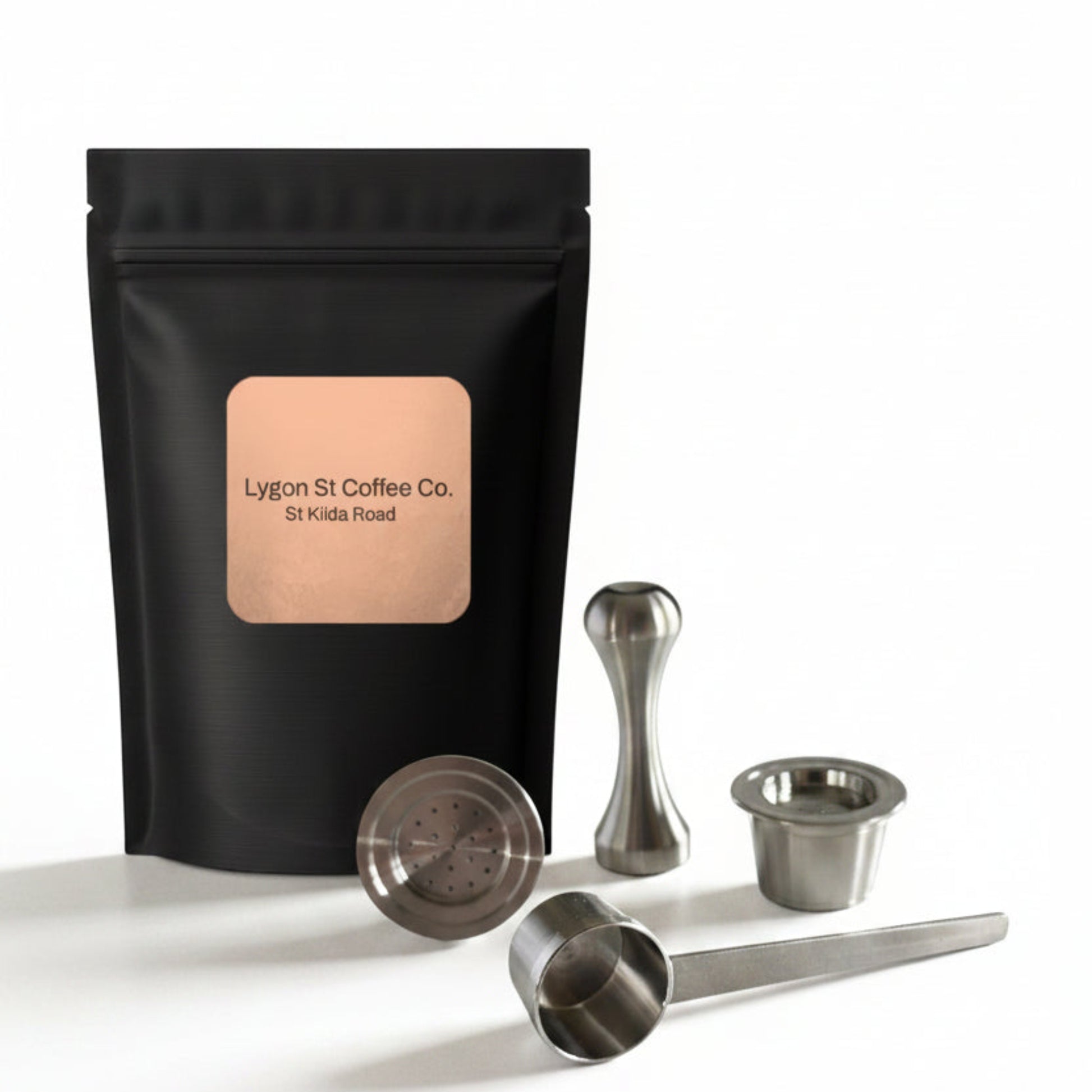 Pod Star starter pack for Espressotoria coffee machines featuring two refillable stainless steel capsules, an espresso tamper, a measuring scoop, and fresh coffee groundson a white background.