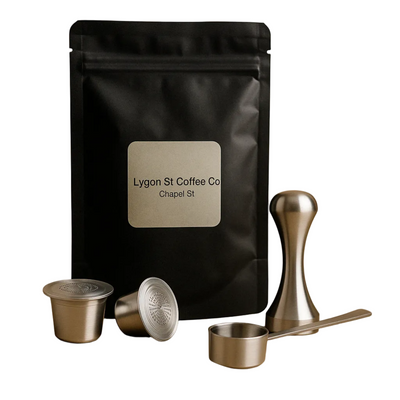 Pod Star starter pack for Nespresso Original line coffee machines featuring two refillable stainless steel capsules, an espresso tamper, a measuring scoop, and fresh coffee grounds on a white background.