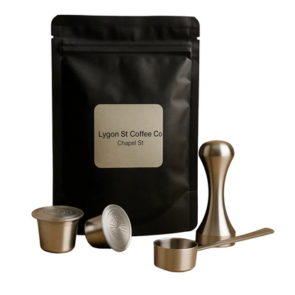 Pod Star starter pack for Nespresso Original line coffee machines featuring two refillable stainless steel capsules, an espresso tamper, a measuring scoop, and fresh coffee grounds on a white background.