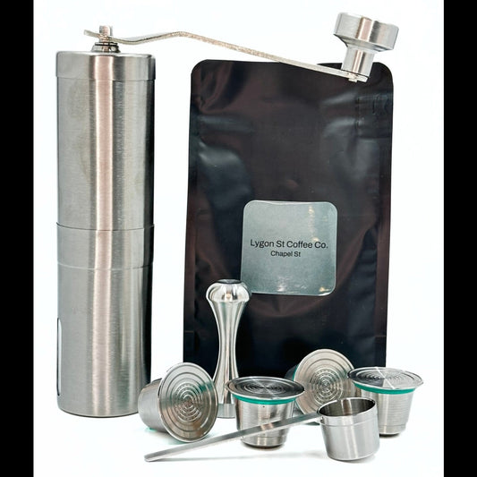 Pod Star ultimate bundle for Nespresso Original line coffee machines featuring four stainless steel reusable capsules, a manual hand grinder, an espresso tamper, and a coffee measuring scoop on a white background.