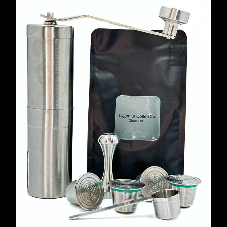 Pod Star ultimate bundle for Nespresso Original line coffee machines featuring four stainless steel reusable capsules, a manual hand grinder, an espresso tamper, and a coffee measuring scoop on a white background.