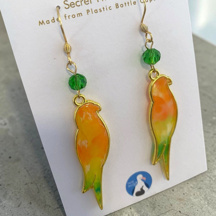 Studio flat lay presentation of the geometric bird-themed recycled jewelry, perfect for sustainable fashion gift collections. Orange and light green variant.