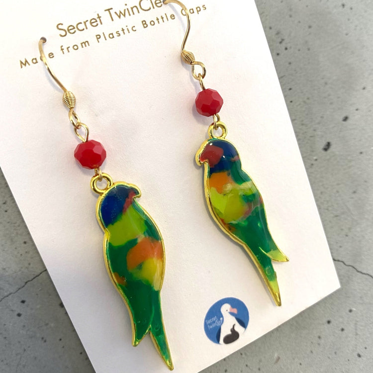 Studio flat lay presentation of the geometric bird-themed recycled jewelry, perfect for sustainable fashion gift collections. Rainbow Lorikeet variant.