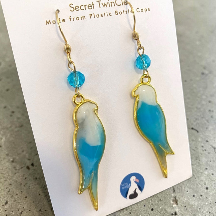 Studio flat lay presentation of the geometric bird-themed recycled jewelry, perfect for sustainable fashion gift collections. Light blue and white variant.